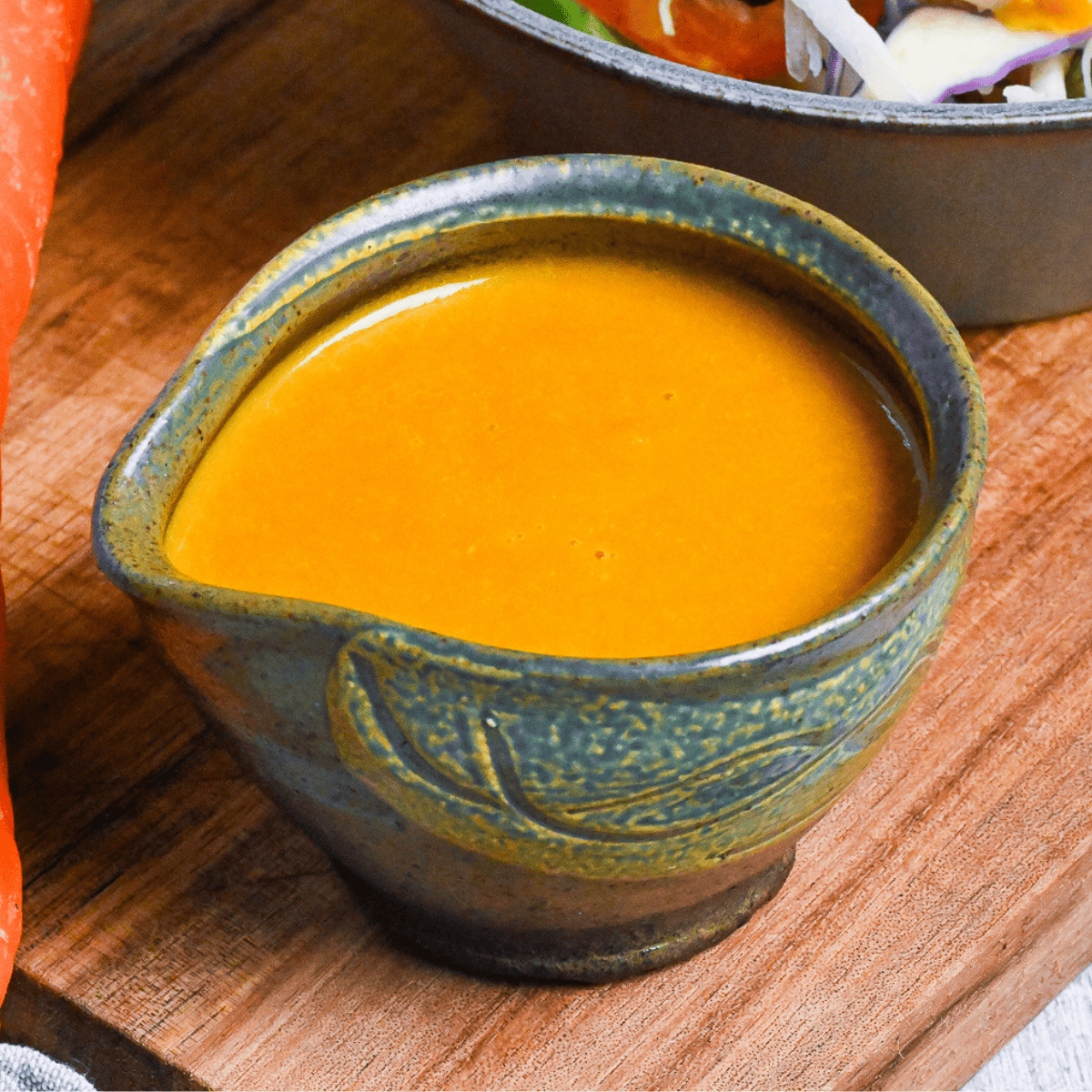 Japanese carrot salad dressing in a small green ceramic jug on a wooden board close up