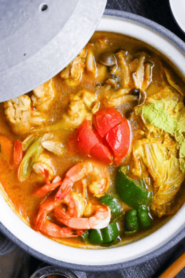 Japanese Curry Hot Pot (Kare Nabe) with chicken, prawns, vegetables and cheese in a gray ceramic pot on a black wood-effect background top down
