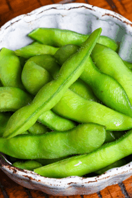 Izakaya style salt boiled edamame in an off-blue bowl on a wooden table with black lines