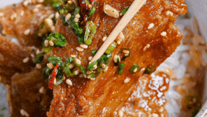 Close up of sauce coated crispy enoki mushrooms held up with wooden chopsticks