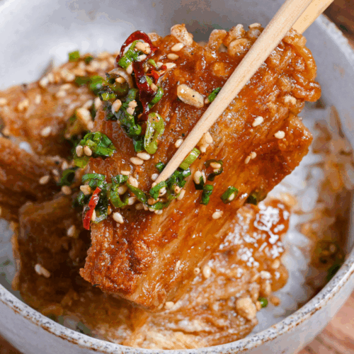 Close up of sauce coated crispy enoki mushrooms held up with wooden chopsticks