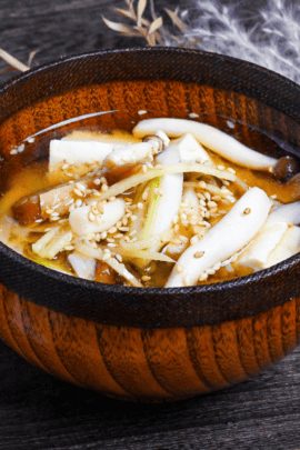 Ginger infused plant-based miso soup sprinkled with sesame seeds in a wooden bowl with brown rim