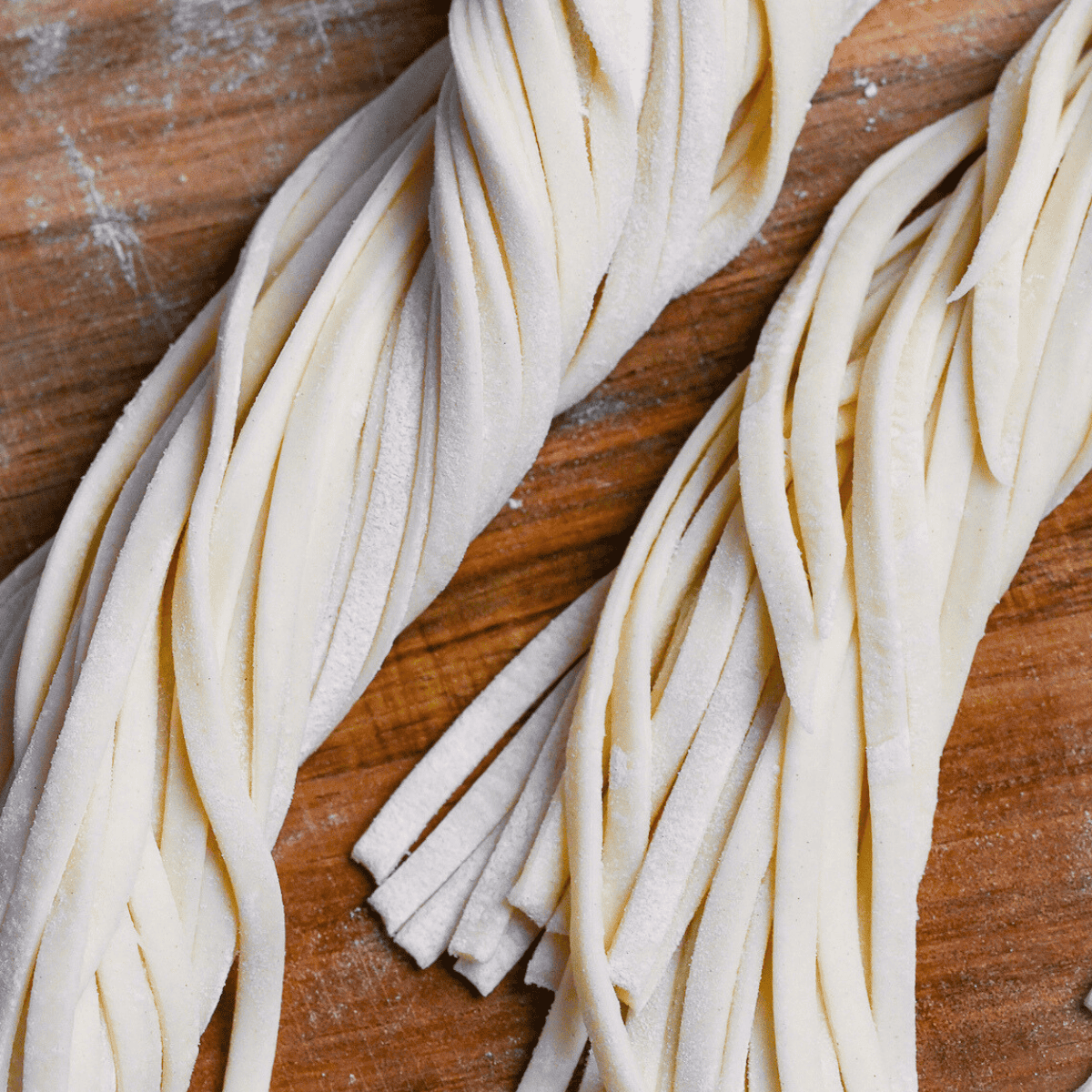 twisted bunch of homemade udon noodles on a floured wooden chopping board
