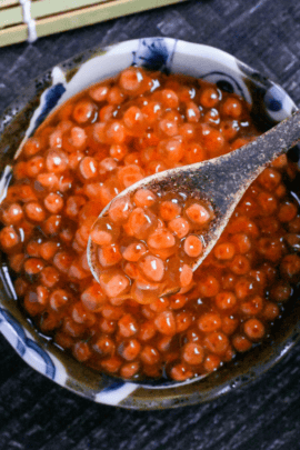 Homemade cured (marinated) salmon roe (ikura) in a small brown bowl and on a brown ceramic spoon