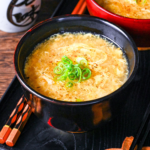 Kakitamajiru (Japanese egg drop soup) topped with chopped green onions and shichimi togarashi served in a black soup bowl on a black tray with wooden chopsticks