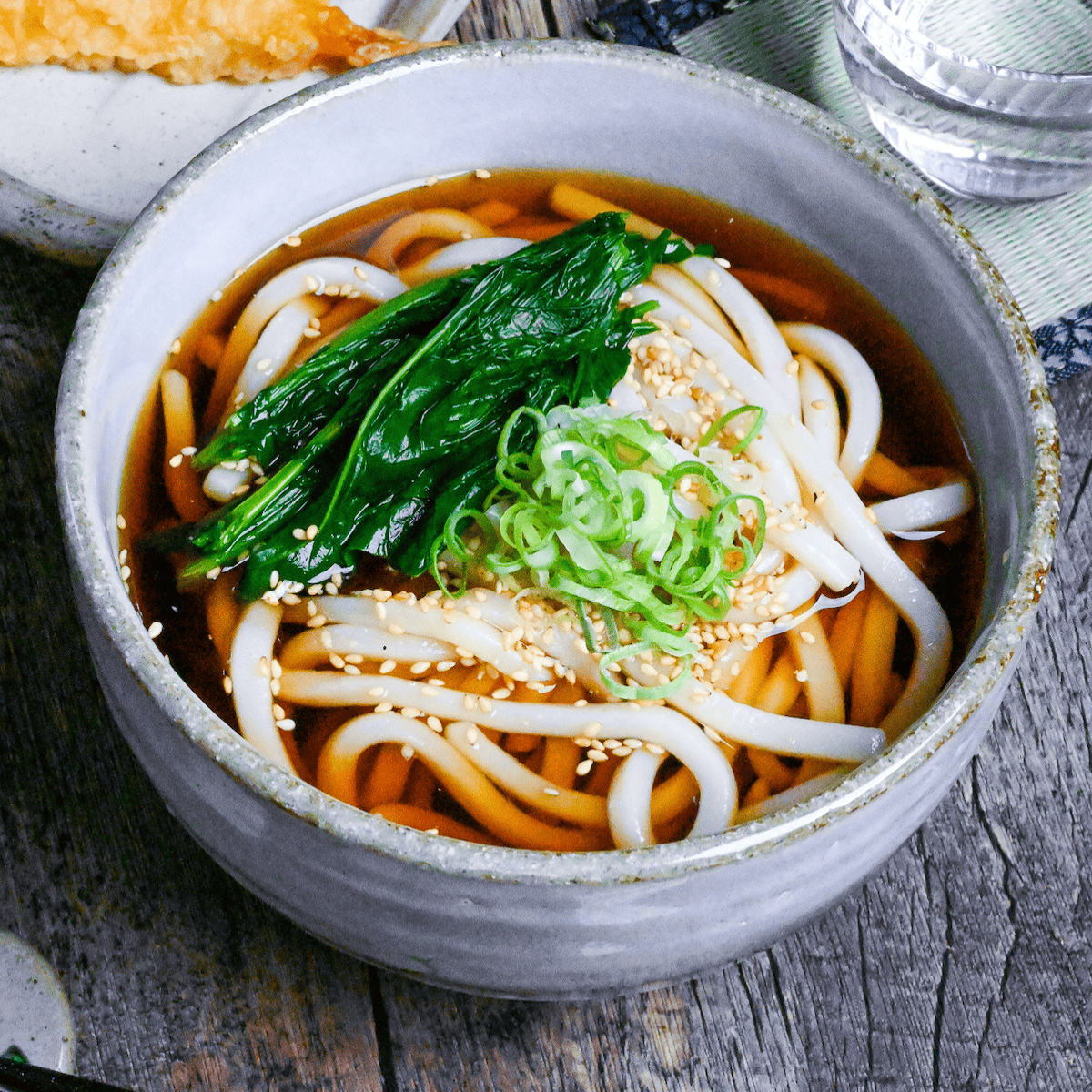 Koro udon topped with blanched spinach, chopped green onions and sesame seeds in a gray ceramic bowl