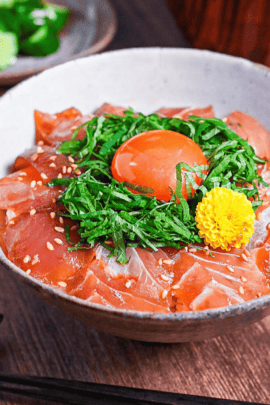maguro zuke don (marinated tuna sashimi bowl) topped with shredded shisho, raw egg yolk and yellow flower next to pickles and miso soup