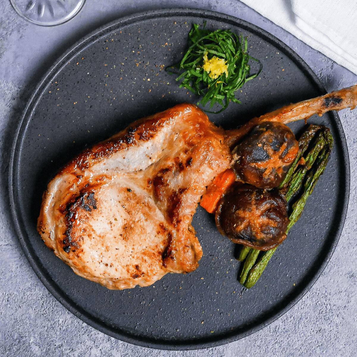 Miso marinated pork chop and roasted vegetables on a dark gray plate with shredded shiso leaves and yuzu peel