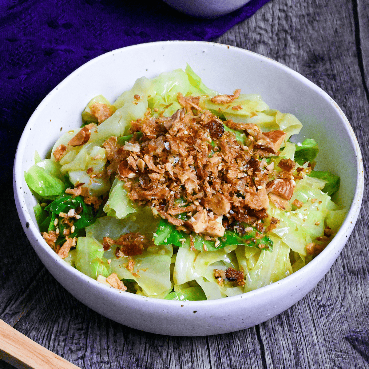 mugen cabbage in a white bowl on ashy wood surface with furikake in a bowl on a blue cloth in the background