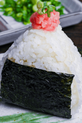 Negitoro onigiri (rice ball) on a gray plate with green brushstroke design, with mashed tuna and chopped green onions in a rectangular plate the background