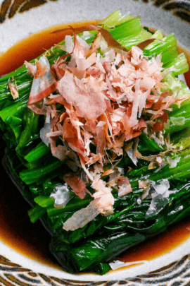 Ohitashi (Japanese spinach salad in dashi) sprinkled with bonito flakes served in a small bowl with brown and gray seigaiha pattern around the edge thumbnail