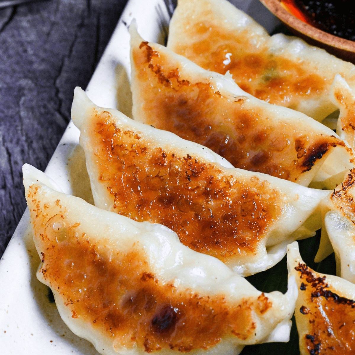 8 pan-fried pork gyoza with crispy base on a cream colored plate