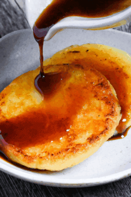pouring sauce over two potato mochi on a small white plate