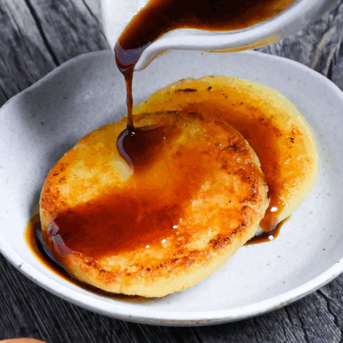 pouring sauce over two potato mochi on a small white plate