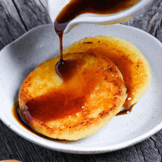 pouring sauce over two potato mochi on a small white plate