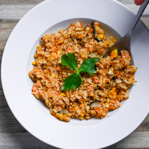 Salmon fried rice served in a white dish and garnished with mitsuba (Japanese wild parsley) with silver spoon