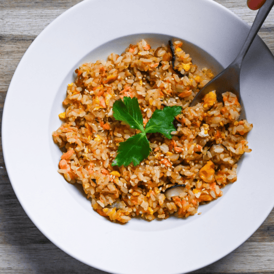 Salmon fried rice served in a white dish and garnished with mitsuba (Japanese wild parsley) with silver spoon