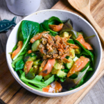 crispy salmon skin salad in a white bowl on a wooden chopping board with a wooden spoon in the background