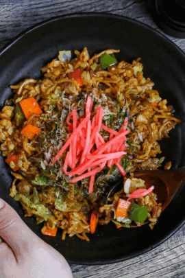 scooping a spoonful of soba-meshi from a black plate next to salt and pepper grinders
