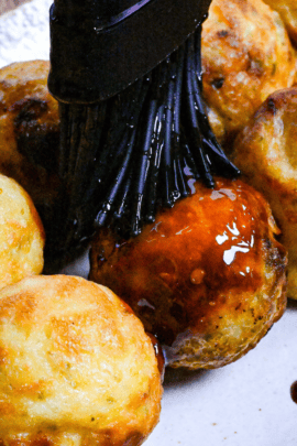 Brushing takoyaki with homemade takoyaki sauce using a black silicone pastry brush