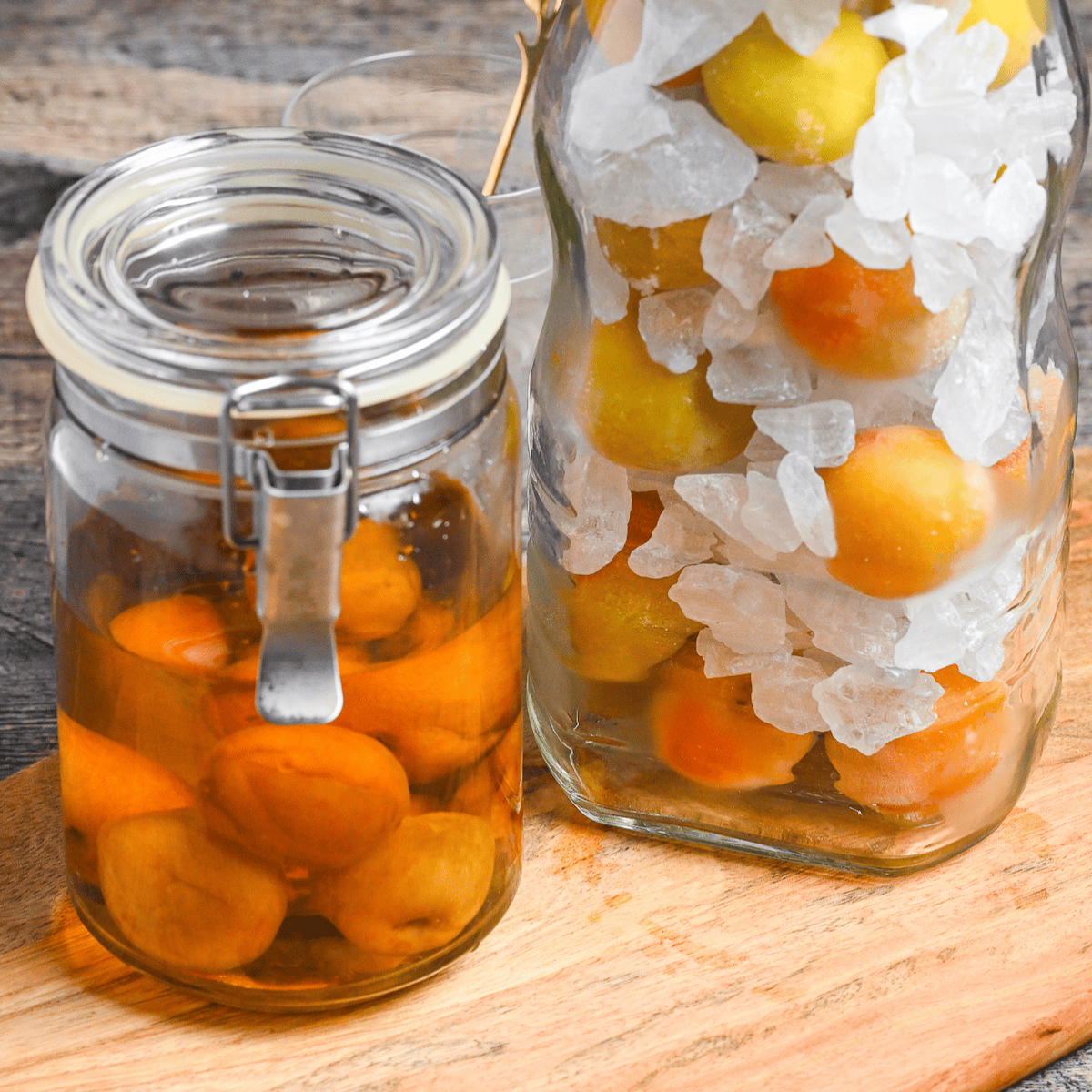 completed ume syrup in a jar next to a jar of ume and rock sugar in layers on a wooden board