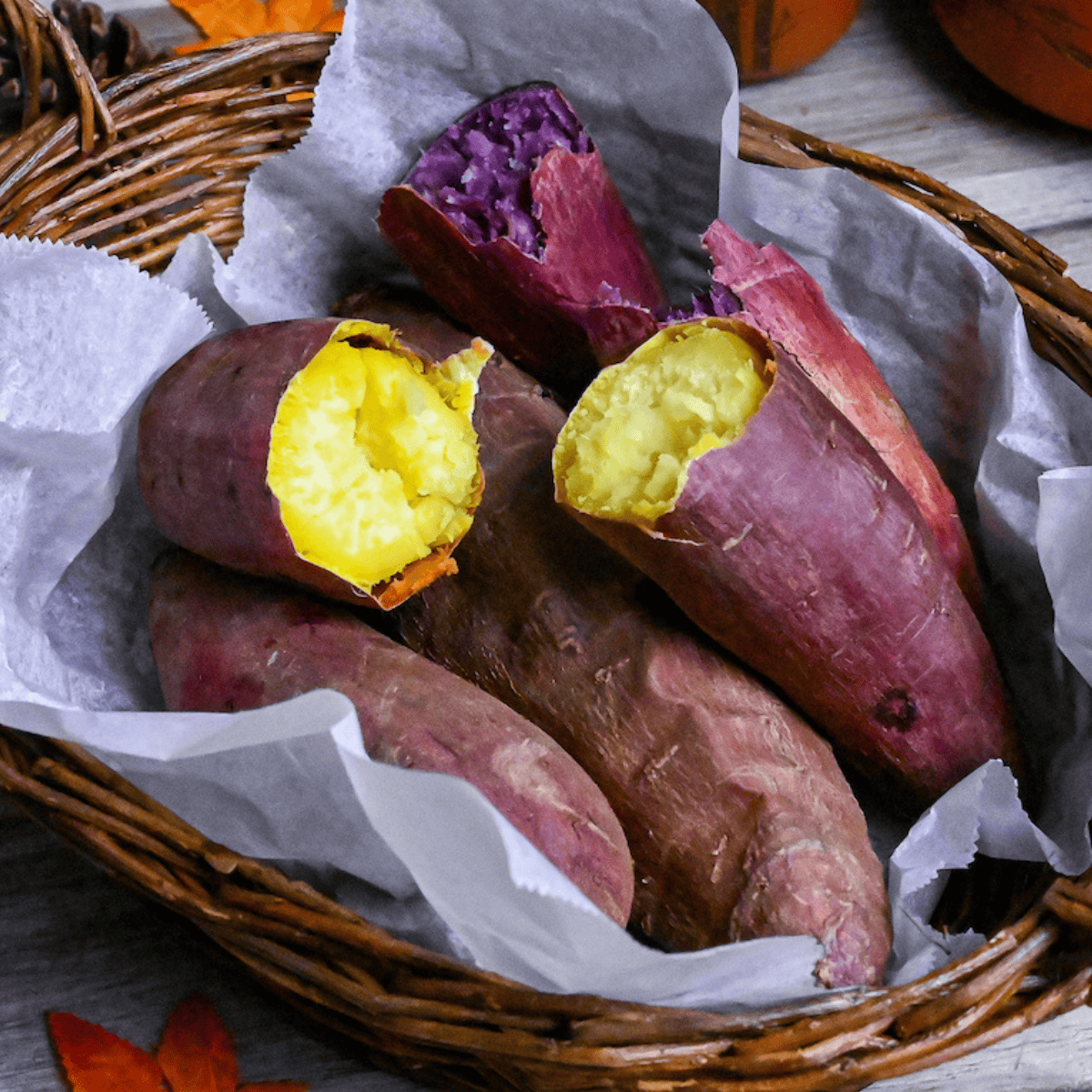 Yaki imo (baked Japanese sweet potatoes) in a woven basket lined with paper and surrounded by pinecones and maple leaves
