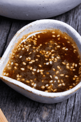 yakiniku restaurant style salad dressing in a small cream ceramic jug with a bowl of salad and wooden salad fork in the background