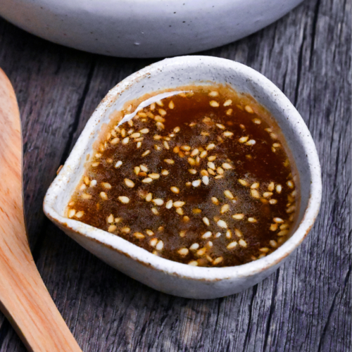 yakiniku restaurant style salad dressing in a small cream ceramic jug with a bowl of salad and wooden salad fork in the background