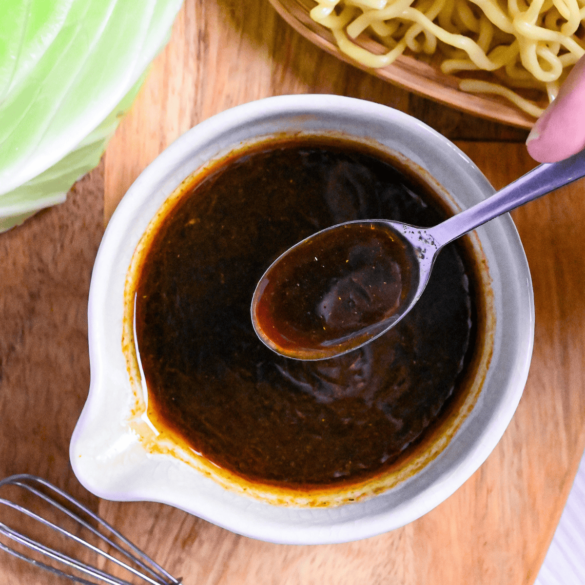 Homemade yakisoba sauce in a small white ceramic jug with silver spoon held above