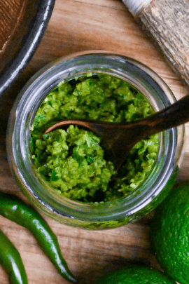 Homemade yuzu kosho made with unripe green yuzu and green chilis in a glass jar on a wooden chopping board